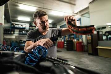 Fototapeta na wymiar Car mechanic using air blow gun while working in auto repair shop.