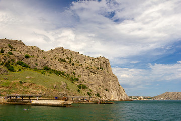 Fototapeta na wymiar Beautiful summer sea landscape at the resort in the Crimea in warm sunny day. Concrete pier in the sea at the foot of the mountain. Seascape.
