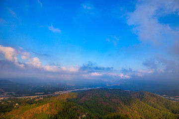 Amazing view from the top of cliff  to the city located on foot of mountains. The rock under fairytale blue sky with the clouds.  Beautiful mountain landscape. Panorama.