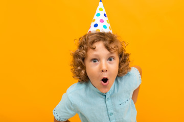 European red-haired curly boy with a festive cap is grimacing at the camera isolated yellow background
