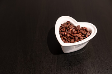 In love with coffee. Coffee is in my heart. Coffee beans in heart shaped bowl on the black desk.