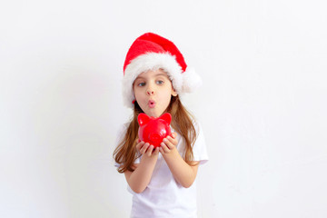 Young child girl in a Santa hat keeps a piggy Bank isolated.