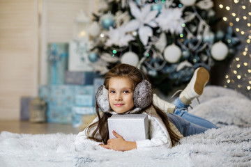 Happy little child girl with gift box sitting near decorated xmas tree with lights. Merry Christmas