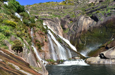 Waterfall with colorful rocks and blue sky. Ezaro cascade, Xallas river. Dumbria, Spain.