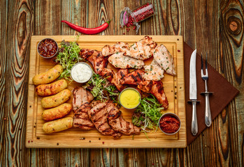 Assorted delicious grilled meat and vegetables with fresh salad and bbq sauce on cutting board on wooden background. Big set of Hot Meat Dishes