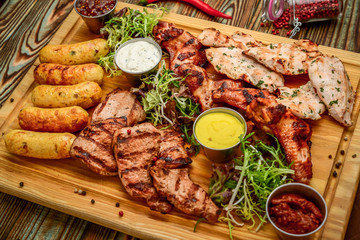 Assorted delicious grilled meat and vegetables with fresh salad and bbq sauce on cutting board on wooden background. Big set of Hot Meat Dishes