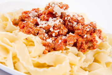 Reginette pasta with bolognese sauce decorated with parmesan on a plate on a white background