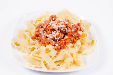 Reginette pasta with bolognese sauce decorated with parmesan on a plate on a white background
