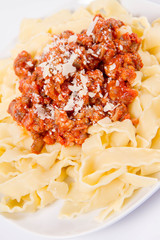 Reginette pasta with bolognese sauce decorated with parmesan on a plate on a white background
