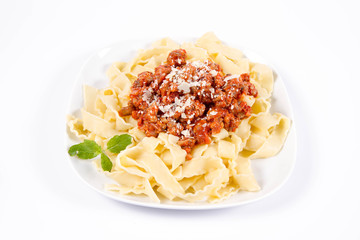 Reginette pasta with bolognese sauce decorated with parmesan and fresh herbs on a plate on a white background