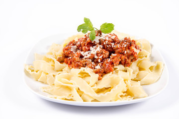 Reginette pasta with bolognese sauce decorated with parmesan and fresh herbs on a plate on a white background