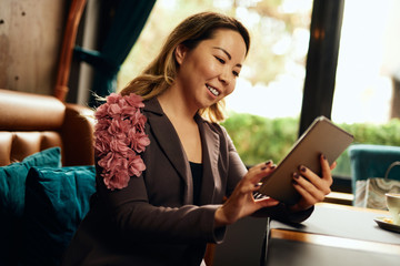 Beautiful Asian woman in a cafe looking at her tablet and smiling 