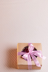 A square gift box with a pink ribbon on a light pink background. Cupcakes inside. Space for text, view from above. vertical photo