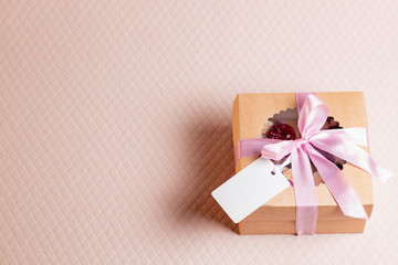 A square gift box with a pink ribbon on a light pink background. Cupcakes inside. Space for text, empty note tied over.