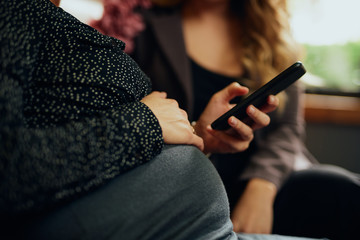 Close up of a pregnant belly and woman holding her phone