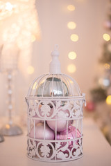 Christmas toys balls silver blue pink in white openwork cage on the background of Christmas lights.