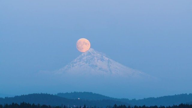 A full moon rising over a snow capped mountain peak. Mount Hood, Oregon.