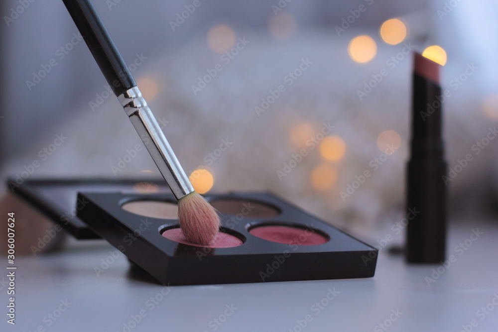 Wall mural closeup of makeup brush and eyeshadow palette with fairy lights in the background. concept of winter