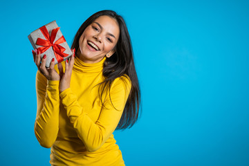 Pretty woman received gift box and interested in what's inside. She is happy and flattered by attention. Girl on blue background.