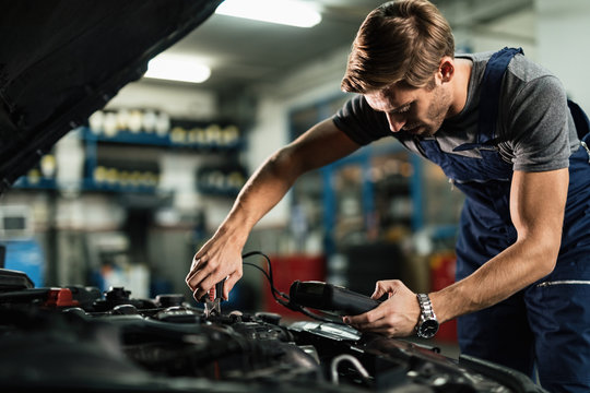 Auto mechanic using diagnostic tool while repairing car engine in a workshop.
