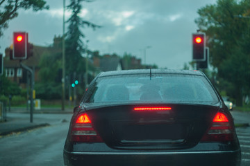 Rear view of a car, displaying stop ligths and red lights, traffic signals, at dusk, in poor visibility conditions. Concept photo, with shallow depth of field and toned colors.