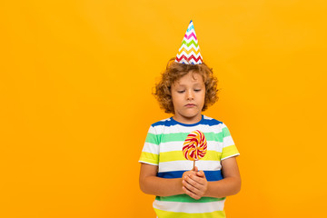 European red-haired curly-haired boy in a striped T-shirt with candy isolated over yellow background