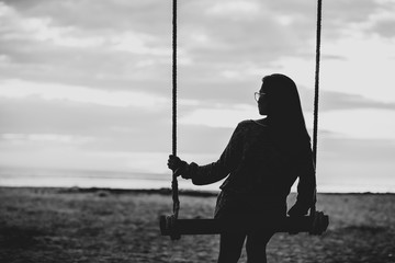 Single woman alone sitting  swinging on the beach sunset.are Lonely. style abstract black and white