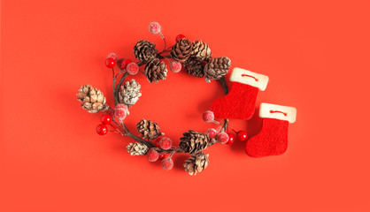 Christmas. New Year. Festive wreath of fir cones, red berries and red boots. Festive mood. Scenery on a red background.