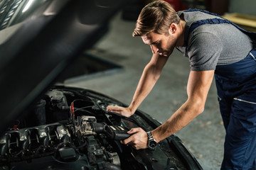 Fototapeta na wymiar Young car mechanic using diagnostic tool while working in auto repair shop.