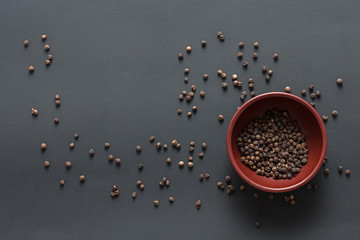 Pepper mill with copper inserts on black background with some black pepper in a clay bowl.
