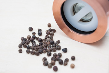 Black pepper mill with copper inserts on white background with some pepper around.
