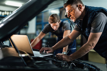 Fototapeta Auto mechanic using laptop while working on car diagnostic with his coworker. obraz