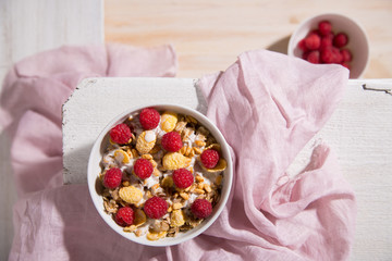 Bowl of granola with yogurt and raspberry on a white wooden background