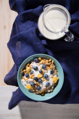 Bowl with oatmeal, blueberries and a jug of milk on a white wooden background