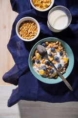 Bowl with oatmeal, corn flakes, blueberries and a glass of milk on a white wooden background