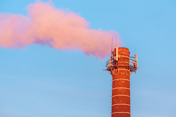 Chimney by the plant with steam from it at sunset time.