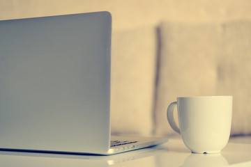 Gray laptop with a white mug on the table in the room. Home business concept. Close up.