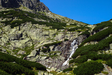 Rocky mountain path with waterfall and blue sky