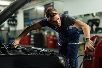Fototapeta na wymiar Young mechanic using AC compressor in auto repair shop.