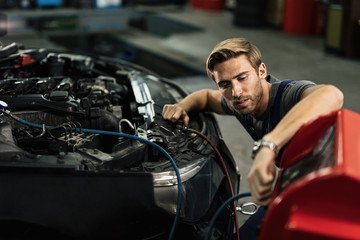 Fototapeta na wymiar Young mechanic maintaining AC unit of a car at auto repair shop.