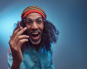 Studio portrait of African Rastafarian male smoking cigarettes. Isolated on a blue background.