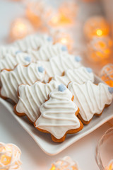 Set of traditional handmade decorated christmas tree shaped gingerbread cookies on the square plate on the windowsill, the christmas light garlands around