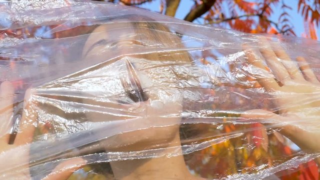 Young woman with short blonde hair can't breathe through a plastic bag, polyethylene wrap. Ecology concept and pulmonary diseases: hypertension, asthma, pneumothorax, hyperventilation syndrome