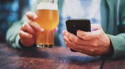 close up of man hand hold smartphone, drinking beer and reading message at bar or pub