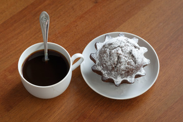 coffee mug and chocolate cupcake on a small plate. On brown wooden background. Side view