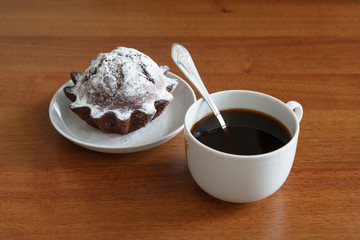 coffee mug and chocolate cupcake on a small plate. On brown wooden background. Side view