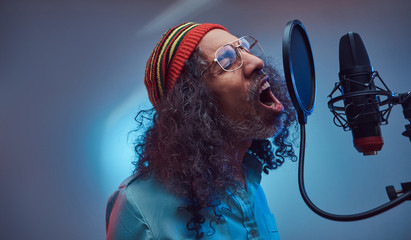 African Rastafarian singer male wearing a blue shirt and beanie emotionally writing song in the...