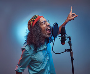 African Rastafarian singer male wearing a blue shirt and beanie emotionally writing song in the...