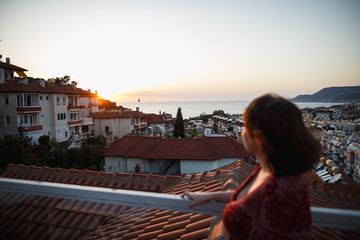 Fototapeta na wymiar Summer outdoor portrait of young pretty sensual girl posing at roof at sunset. Fluing hair on wind. View on mediterranian city buildings and red roofs.
