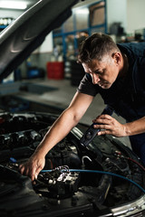 Mid adult mechanic repairing car engine in auto repair workshop.